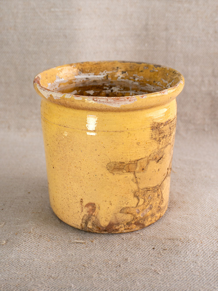 Antique French Provençal confit pot with yellow glaze, wide rim, and aged patina on beige textured fabric.