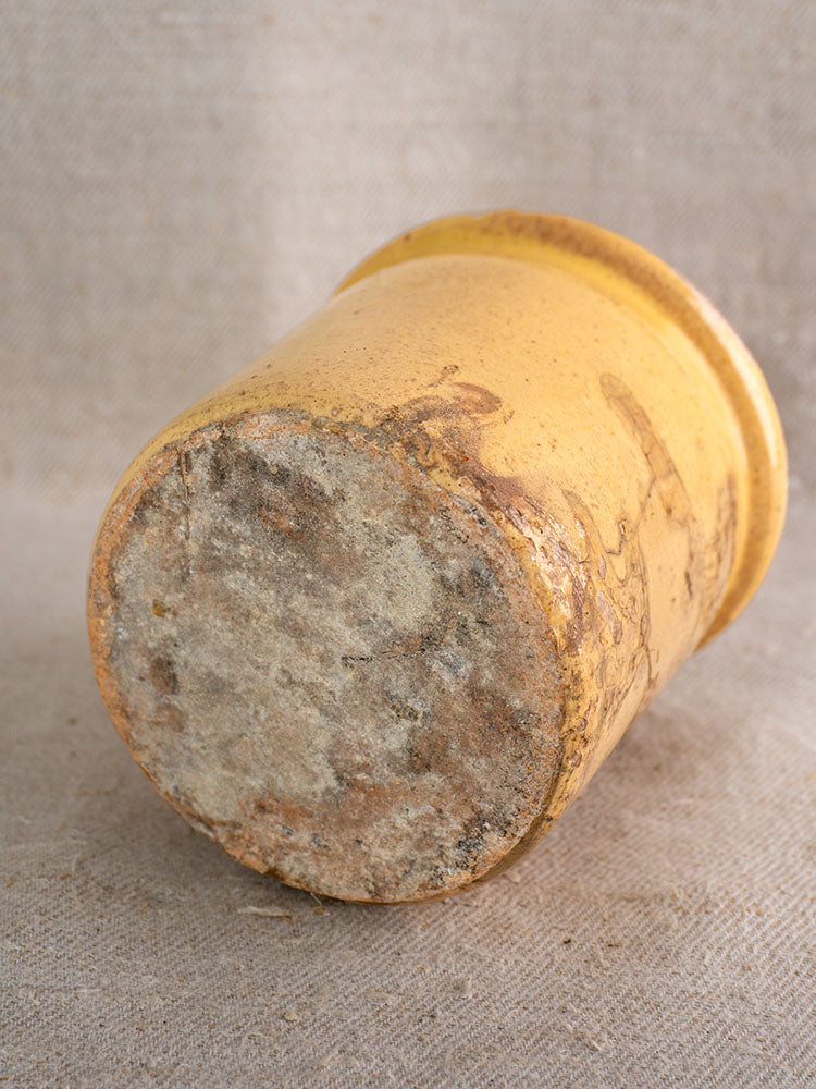 Antique French yellow glazed earthenware confit pot with worn base on textured beige fabric background.
