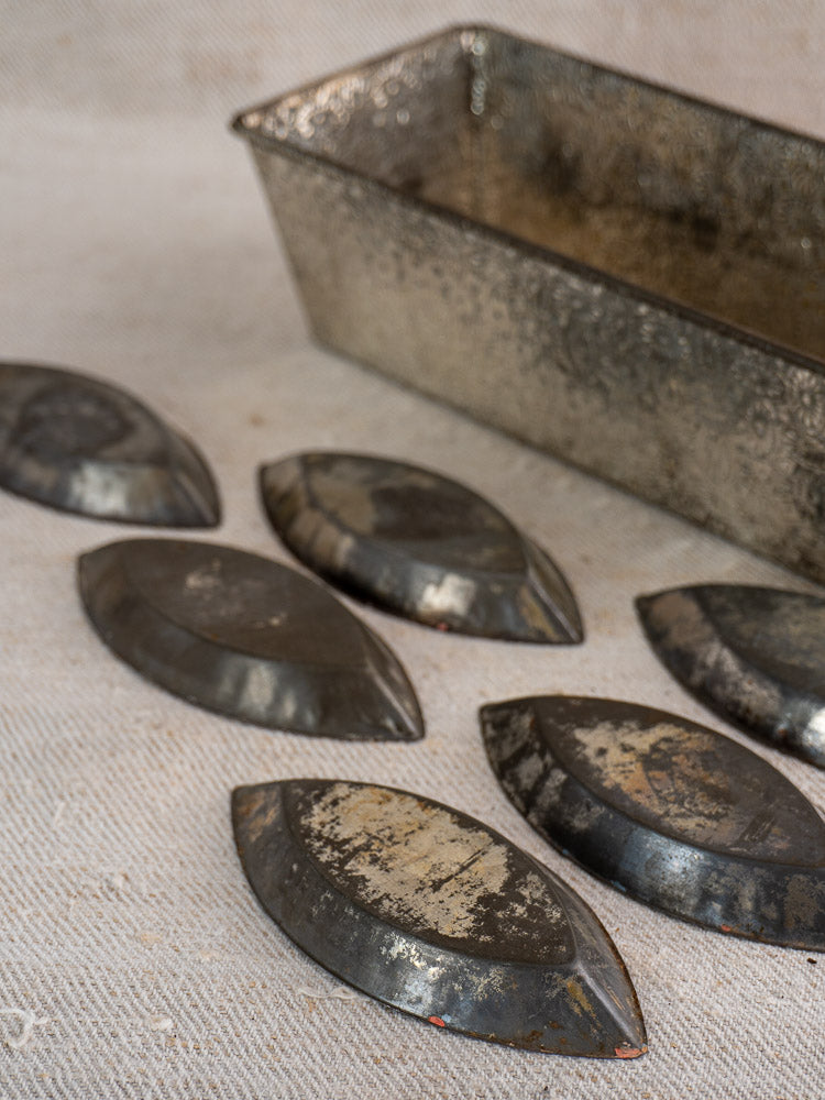 Set of six vintage French tinned steel tartlet molds with patina, on textured fabric, loaf pan behind.
