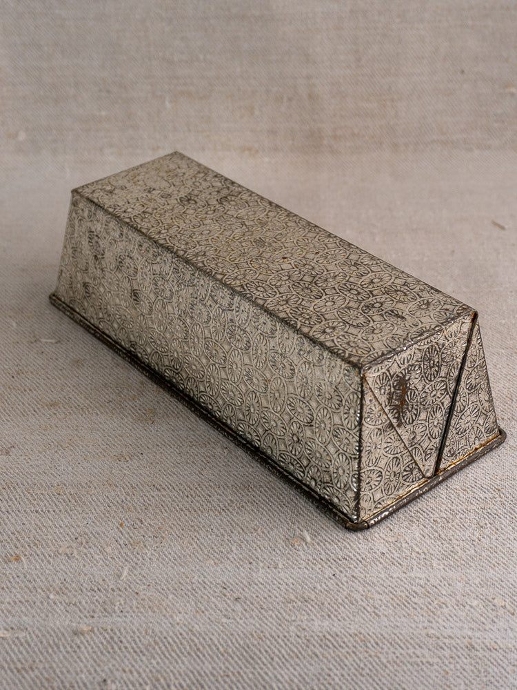 Mid-century French tinned steel box with floral and geometric engravings, sloped sides, and latch on beige fabric.