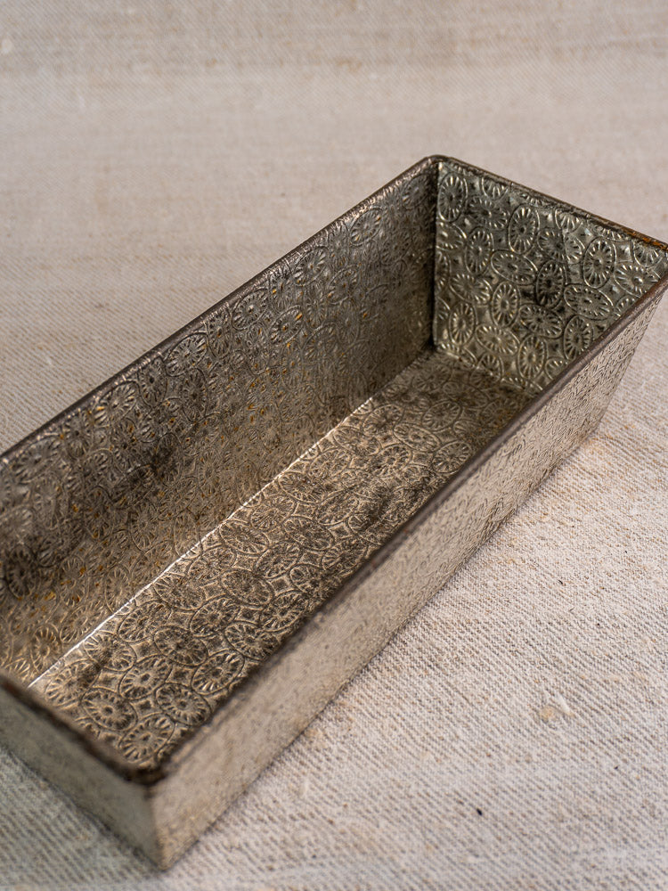 Mid-century tinned steel French loaf pan with ornate embossed interior on textured beige fabric.