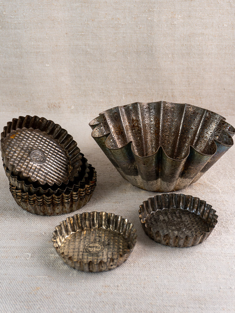 Mid-century tinned steel French bakery molds, large and small, displayed on neutral textured fabric.