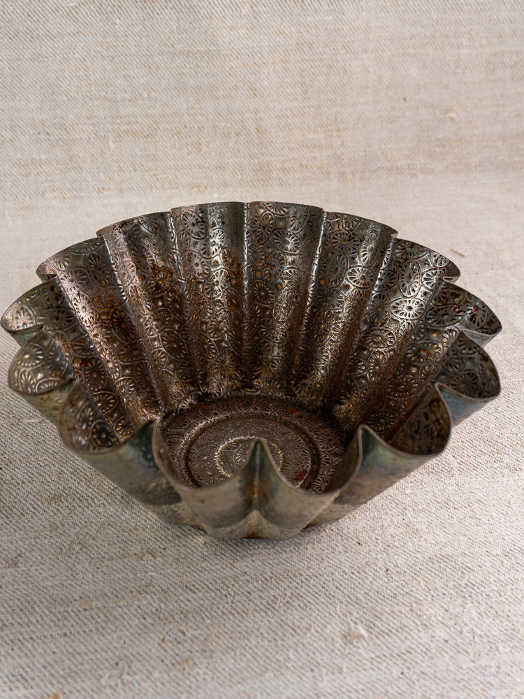Mid-century French tinned steel baking mold with floral fluted design, on a light textured fabric backdrop.