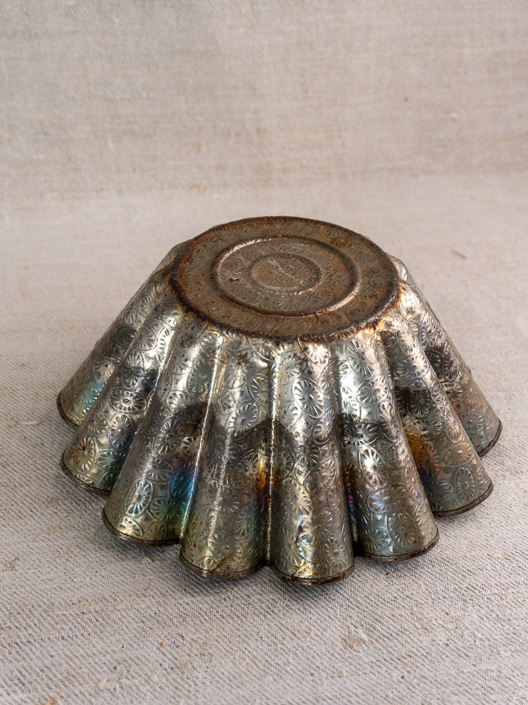Mid-20th-century French tinned steel fluted baking mold with embossed floral design, classic patina on beige fabric.