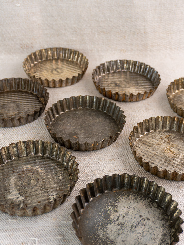Set of eight mid-century French tinned steel baking molds with fluted edges and antique patina on neutral fabric.