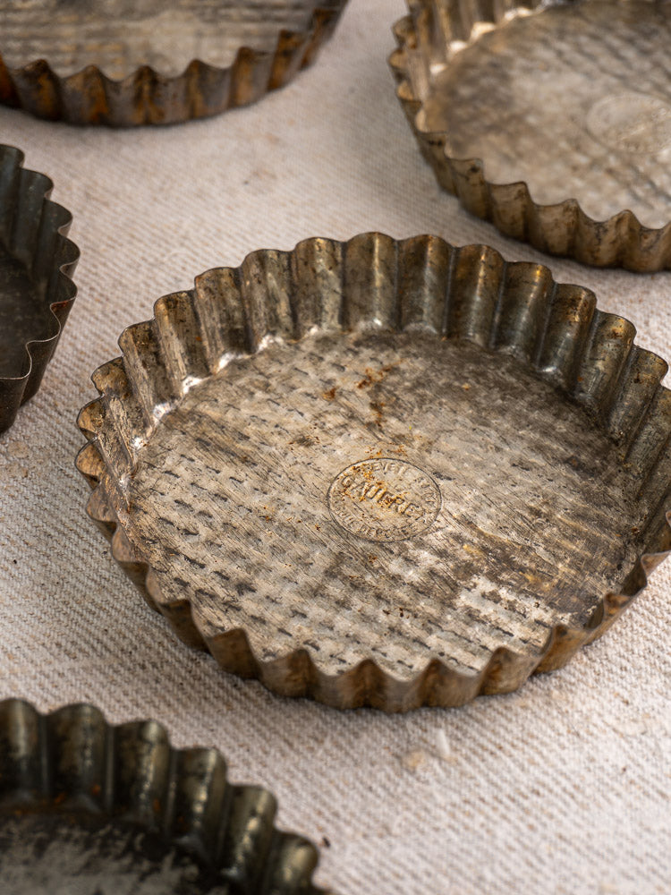 Mid-century tinned steel French baking molds with fluted patina on textured fabric background.