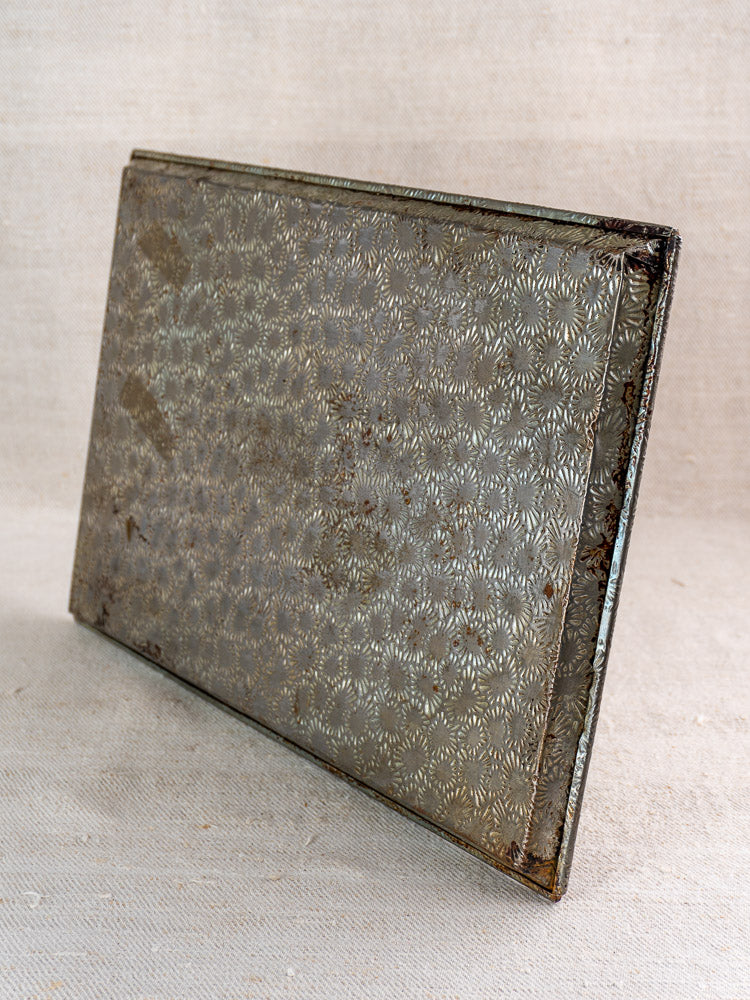 Mid-century French tinned steel box with embossed floral motif, shown upright on beige fabric against a neutral backdrop.