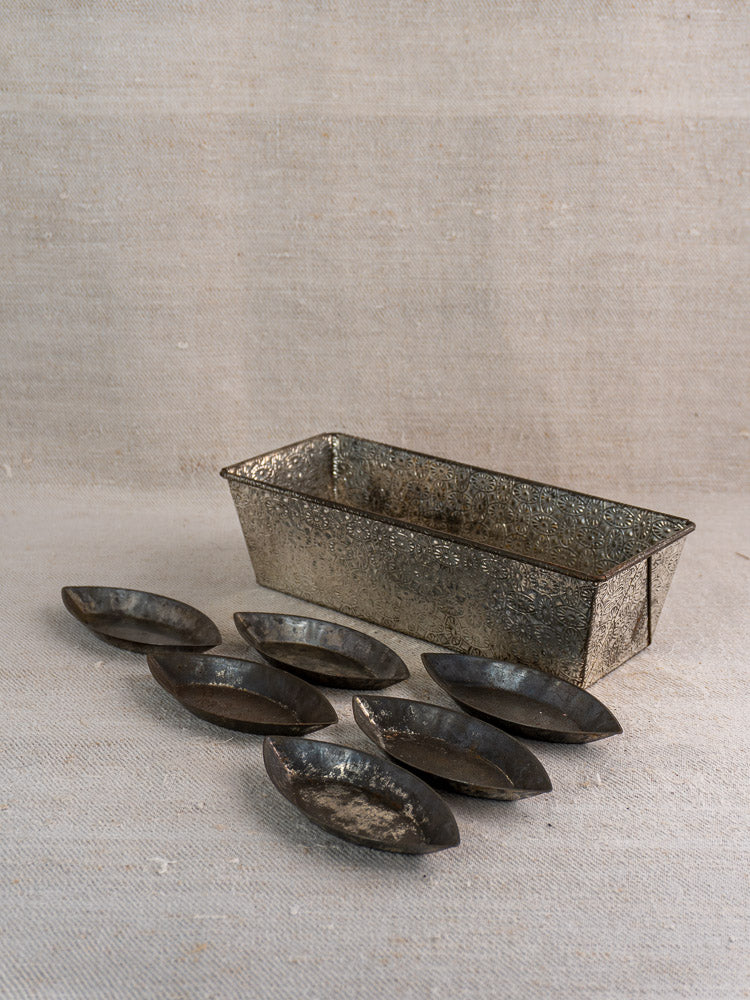 Mid-century French tinned steel rectangular baking pan with seven oval tartlet molds on neutral fabric background.