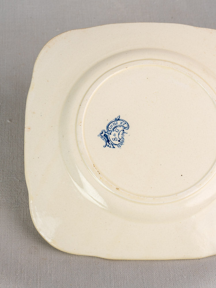 Back of cream Louis XV Terre de Fer plate, Clairefontaine c.1885, blue “S” mark, on textured gray surface.