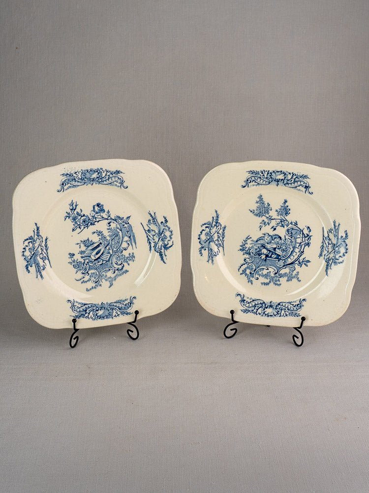 Set of 10 antique French Clairefontaine plates with ornate blue floral and bird designs, upright on black stands.