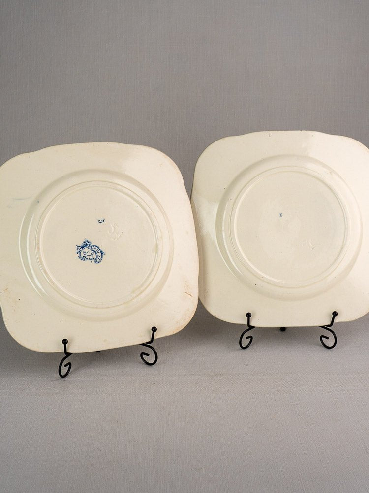 Two off-white square ceramic Clairefontaine plates, Louis XV pattern marks visible, on gray background.
