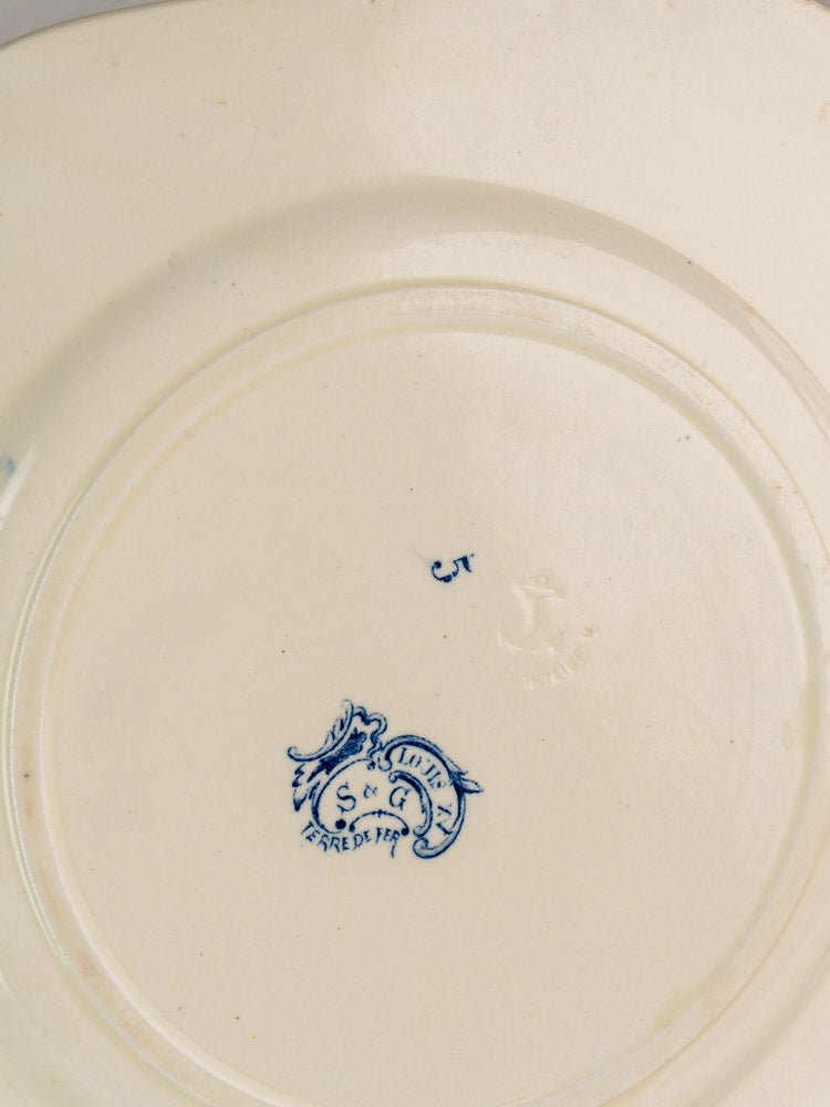 Underside of cream ceramic plate with blue griffin mark and “St. Louis France” inscription.