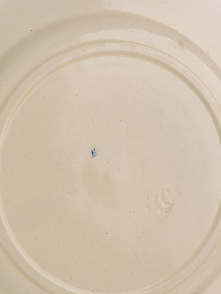 Antique French Clairefontaine plate with cream ceramic surface, blue center mark, and faint embossed detail.