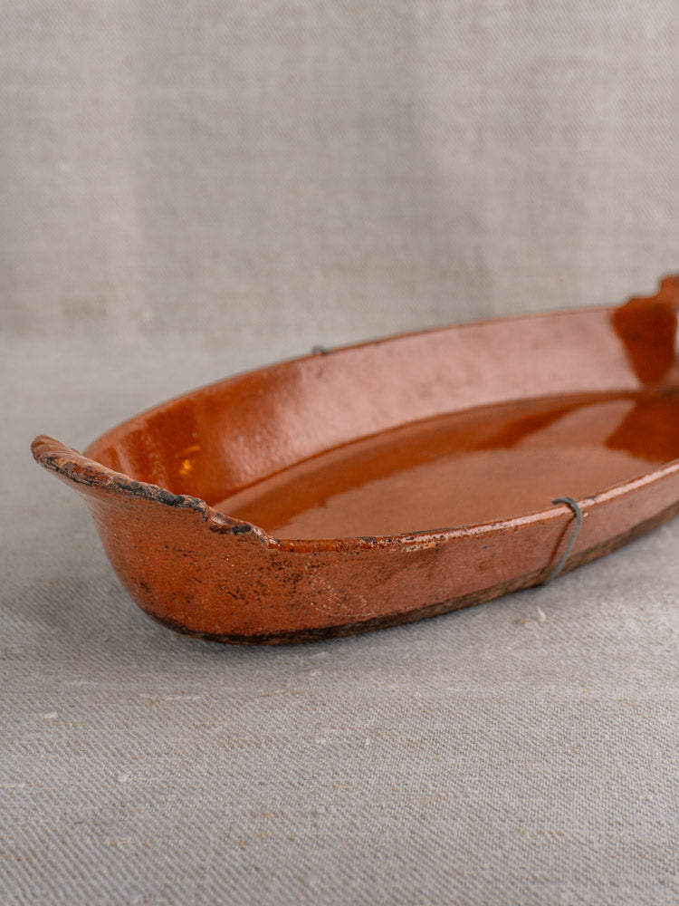 Late 19th-century Saint-Uze Revol antique French baking dish in rustic brown terre vernissée, with wire repair, on beige fabric.