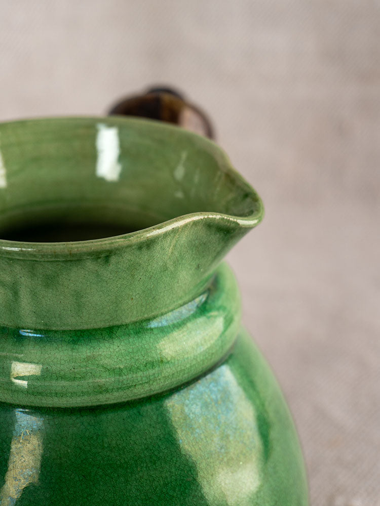 Antique French Dieulefit pitcher, late 19th century, green glazed earthenware, on soft neutral fabric background.