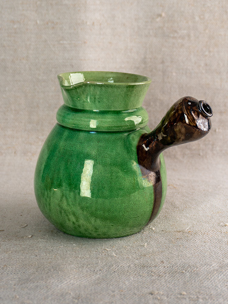 Late 19th century French Dieulefit green glazed earthenware pitcher with wide mouth and angled spout on beige textured fabric.