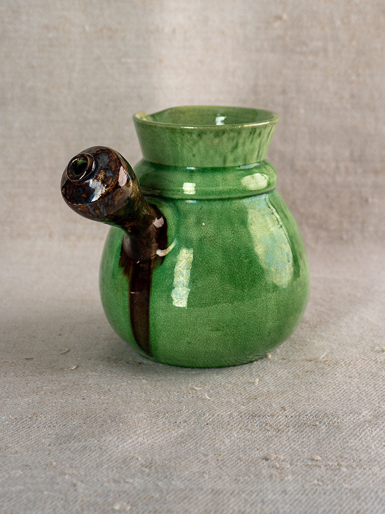 Antique French Dieulefit green glazed earthenware pitcher with round body and spout-neck on neutral textured fabric.