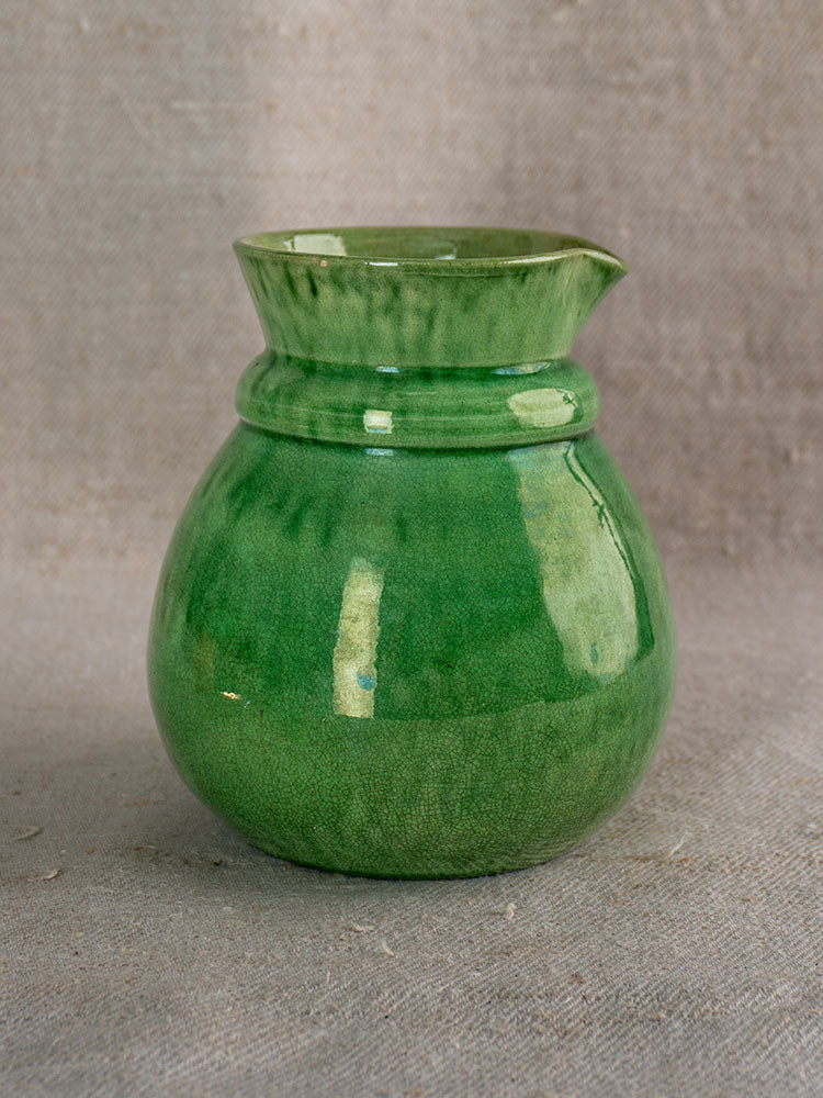 Small green glazed Dieulefit French earthenware pitcher, late 19th century, on textured beige fabric.