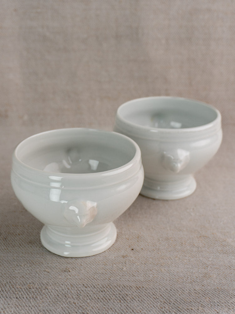Antique French lion head soup bowls in white porcelain, early to mid 20th century, on beige fabric.