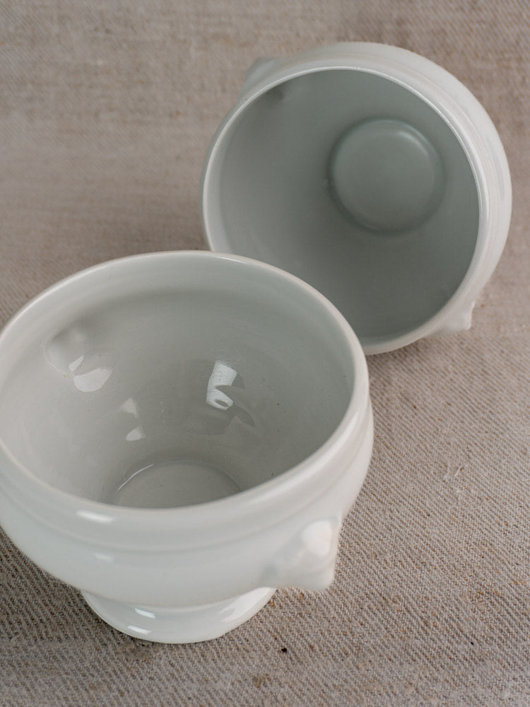 Antique French white porcelain lion head soup bowls, early 20th century, displayed on beige fabric, one tilted showing interior.