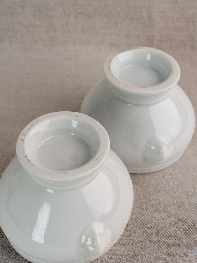 Pair of antique French lion head soup bowls in glossy white porcelain, upside down on beige textured fabric. Early-mid 20th century.