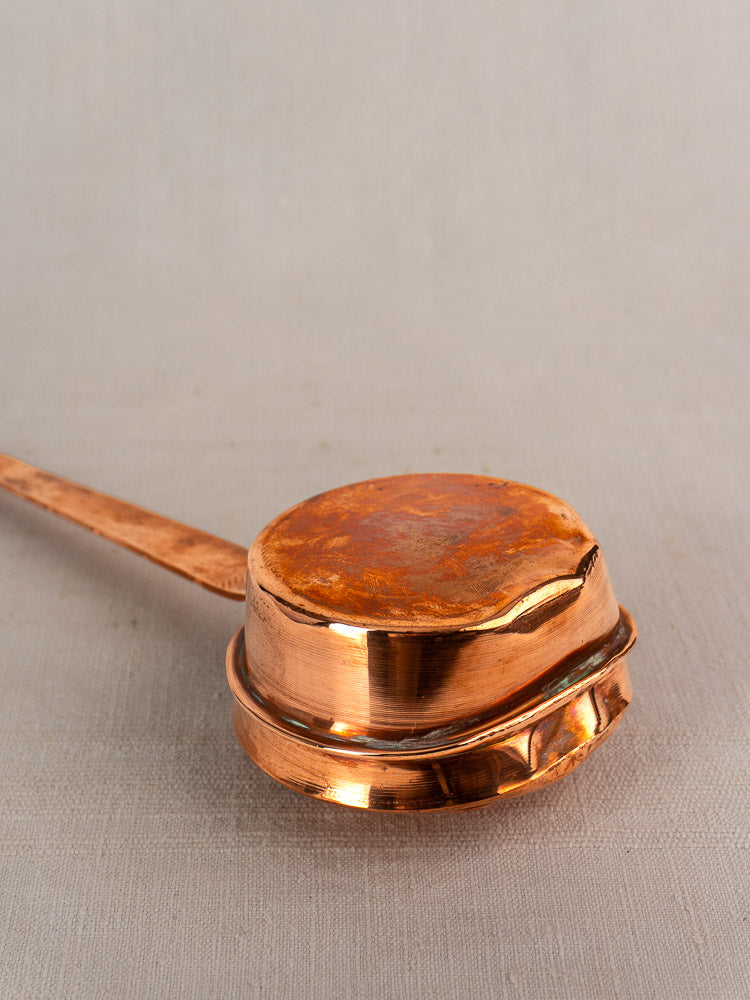 Antique French copper warming pan, late 19th–early 20th c., upside down on neutral fabric, showing dented, tarnished base.