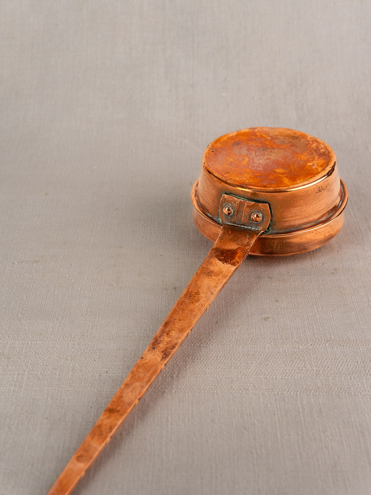 Antique French copper warming pan with riveted handle and weathered patina on a light gray surface.