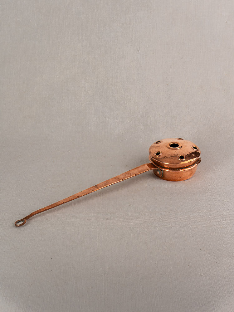 Antique French copper warming pan with long riveted handle, late 19th–early 20th century, on light gray surface.
