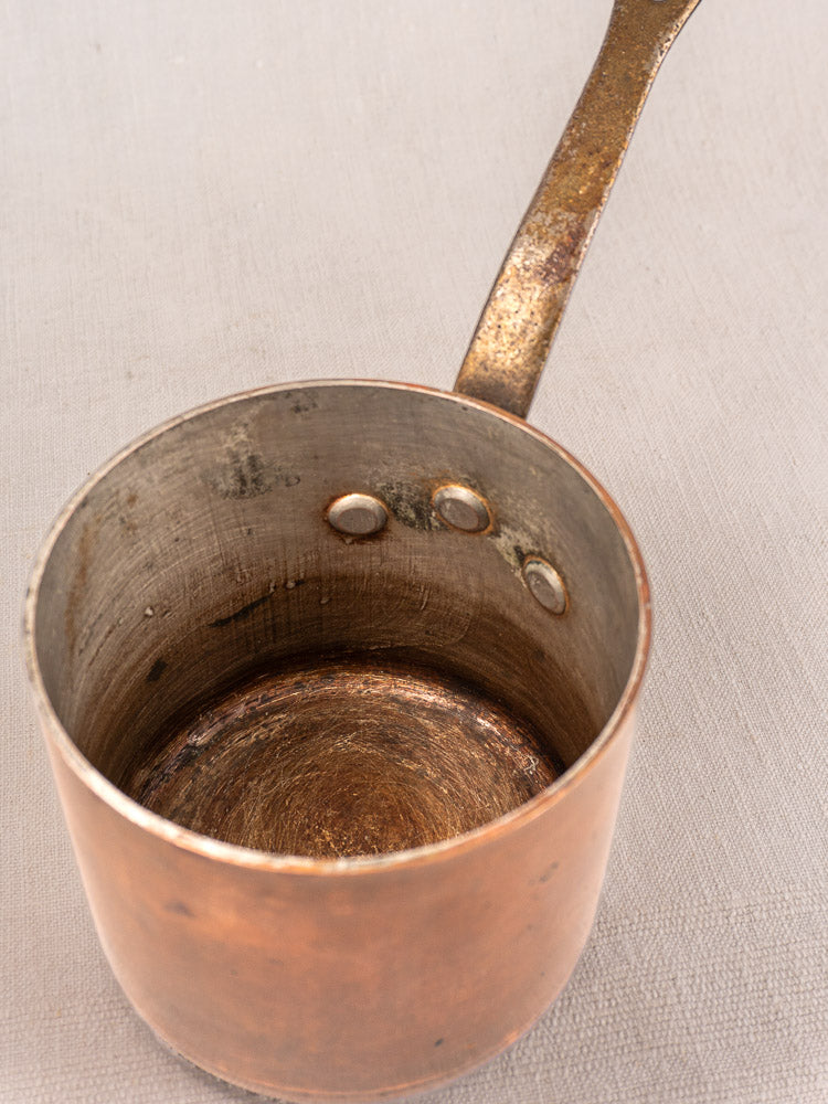 Antique French copper saucepan by Pierre Vergnes Durfort with worn tin interior, single handle, and tarnished patina on pale surface.