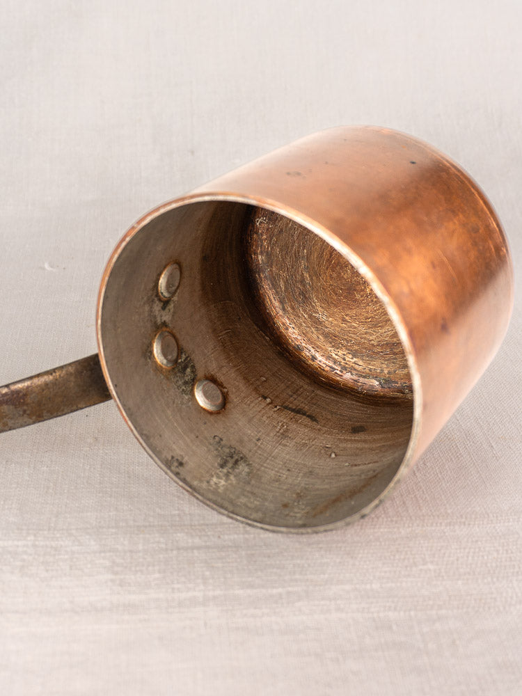 Antique French copper saucepan by Pierre Vergnes Durfort, metal handle, rivets, worn interior, on light surface.
