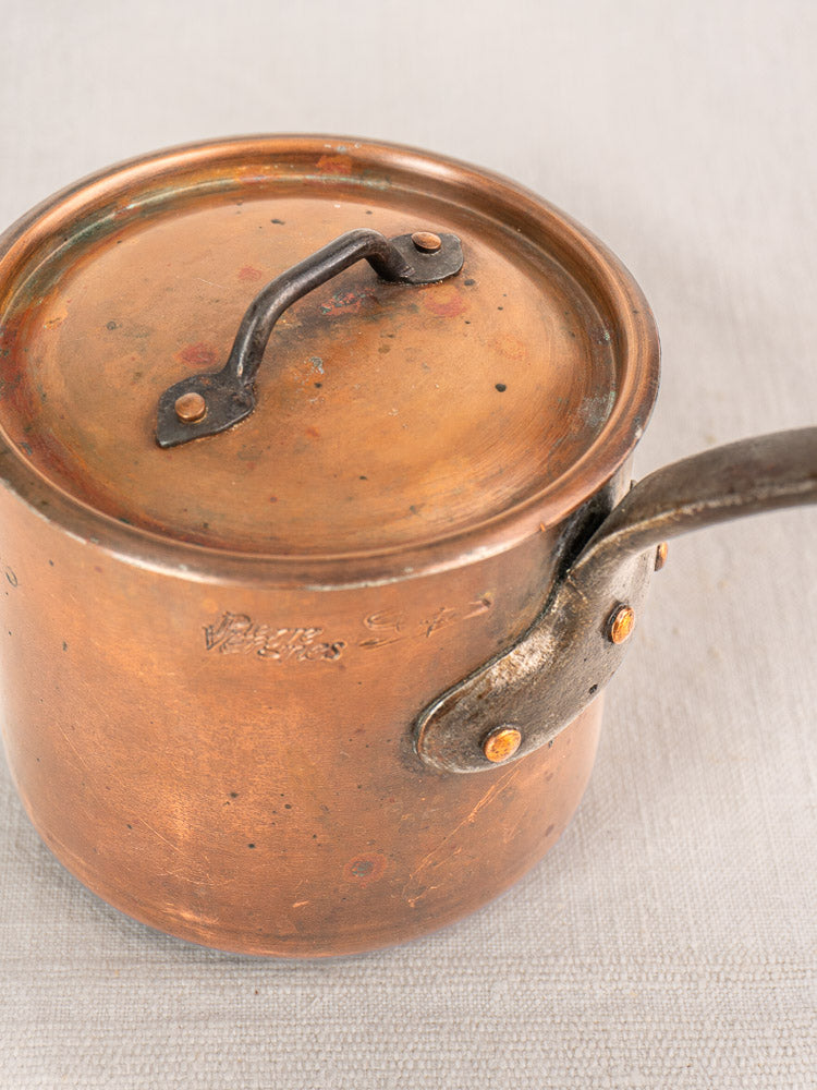 Antique French copper saucepan by Pierre Vergnes Durfort with lid, riveted handle, and visible tarnish on light textured surface.