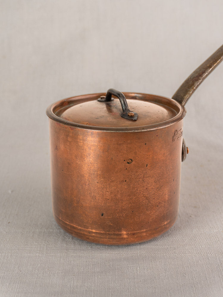 Antique French copper saucepan by Pierre Vergnes Durfort with lid and long handle, gently tarnished on light gray background.