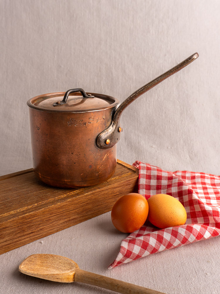 Antique French copper saucepan with lid by Pierre Vergnes Durfort on a wooden board, eggs and spoon nearby.
