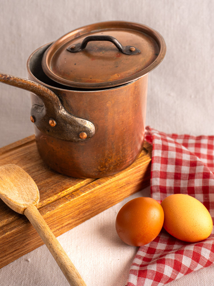 Antique French copper saucepan with lid by Pierre Vergnes Durfort on wooden board with spoon and eggs.