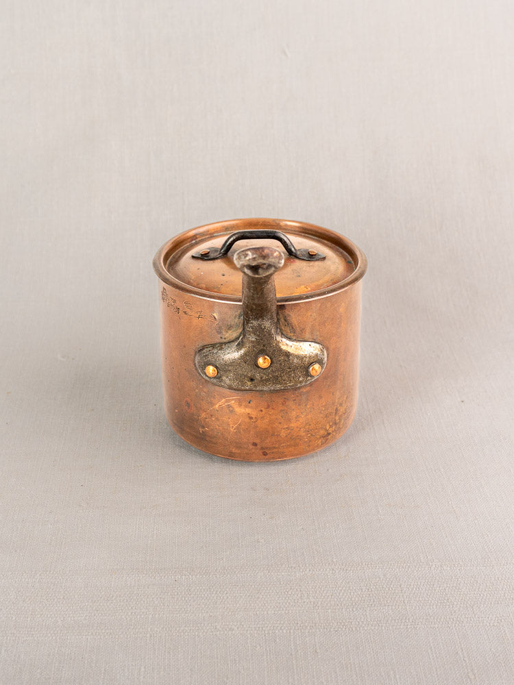 Antique French copper saucepan by Pierre Vergnes Durfort with lid, aged patina, on light fabric background.