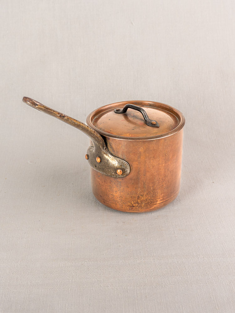 Antique French copper saucepan by Pierre Vergnes Durfort with lid and worn handle on gray textured surface.