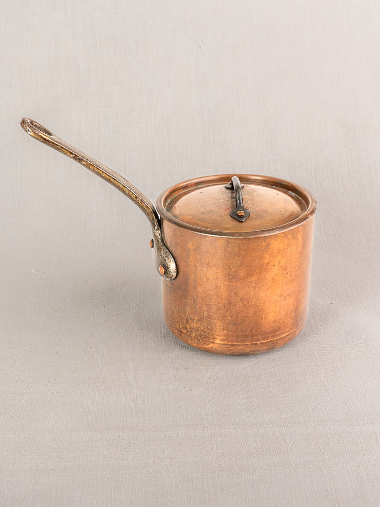 Antique French copper saucepan by Pierre Vergnes Durfort with lid and long curved handle on a light gray surface.