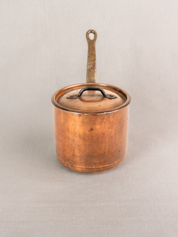 Antique French copper saucepan by Pierre Vergnes Durfort with lid and single handle on light grey fabric.