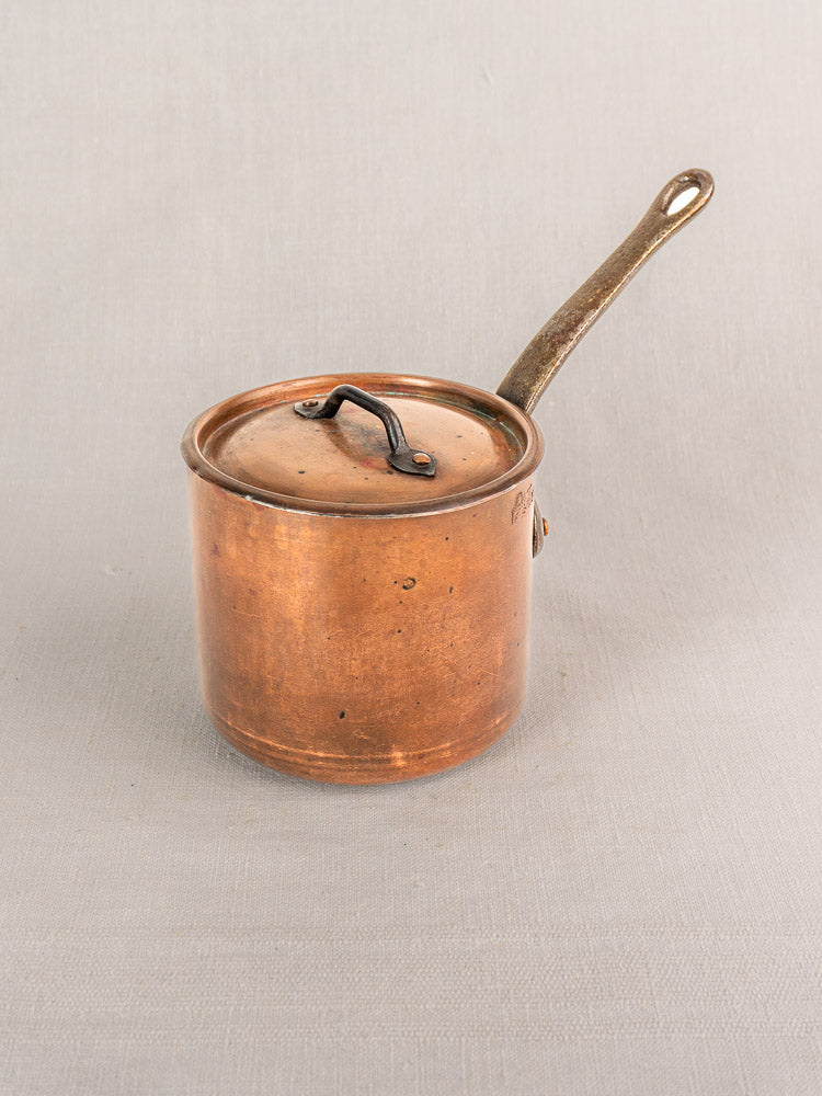 Antique French copper saucepan by Pierre Vergnes Durfort with lid and long handle on light grey surface.