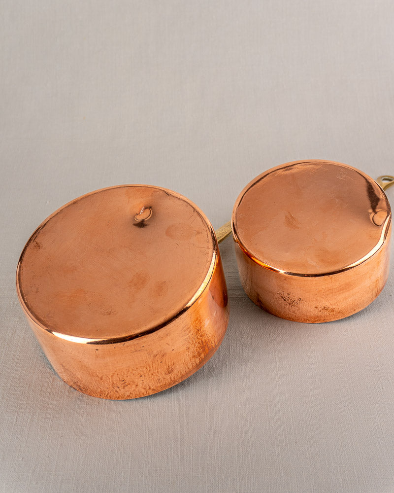 Pair of early 20th-century French copper saucepans, tinned interiors, minor marks, on gray surface.