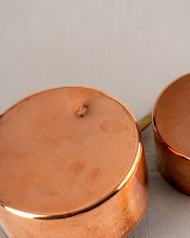 Two upside-down antique French tinned copper saucepans, one with a dent and scorch mark, vintage cookware charm.