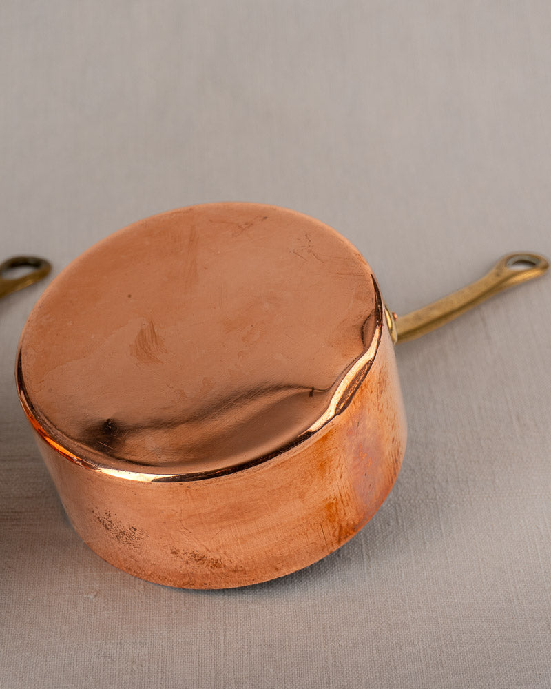 Antique French copper saucepan set of five with brass handles, displayed upside down on a light gray surface.