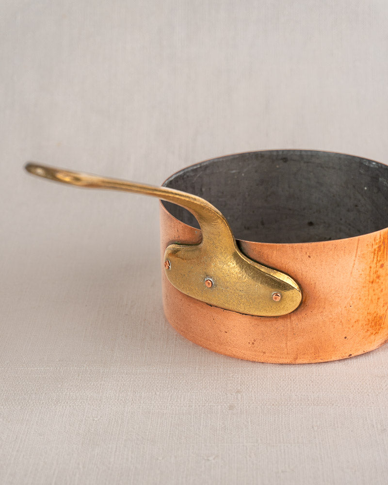Set of five antique French copper saucepans with brass handles and tinned interiors on neutral fabric background.