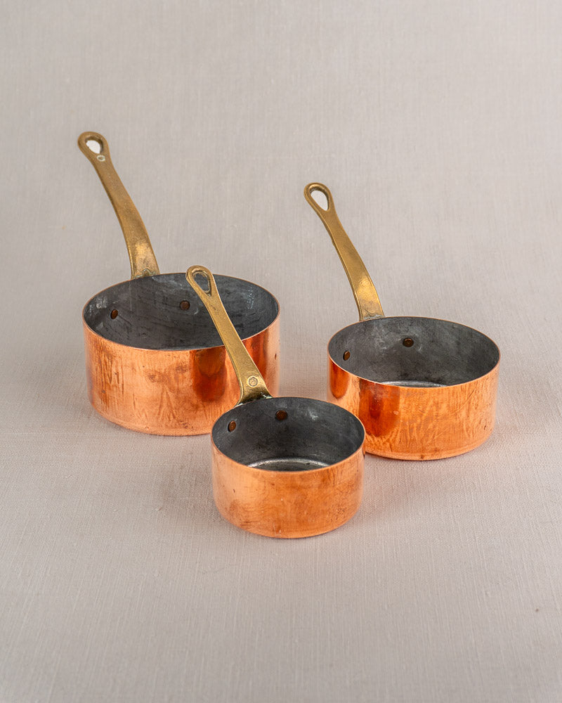 Antique French copper saucepan set of five with brass handles, tinned interiors, displayed on a neutral background.