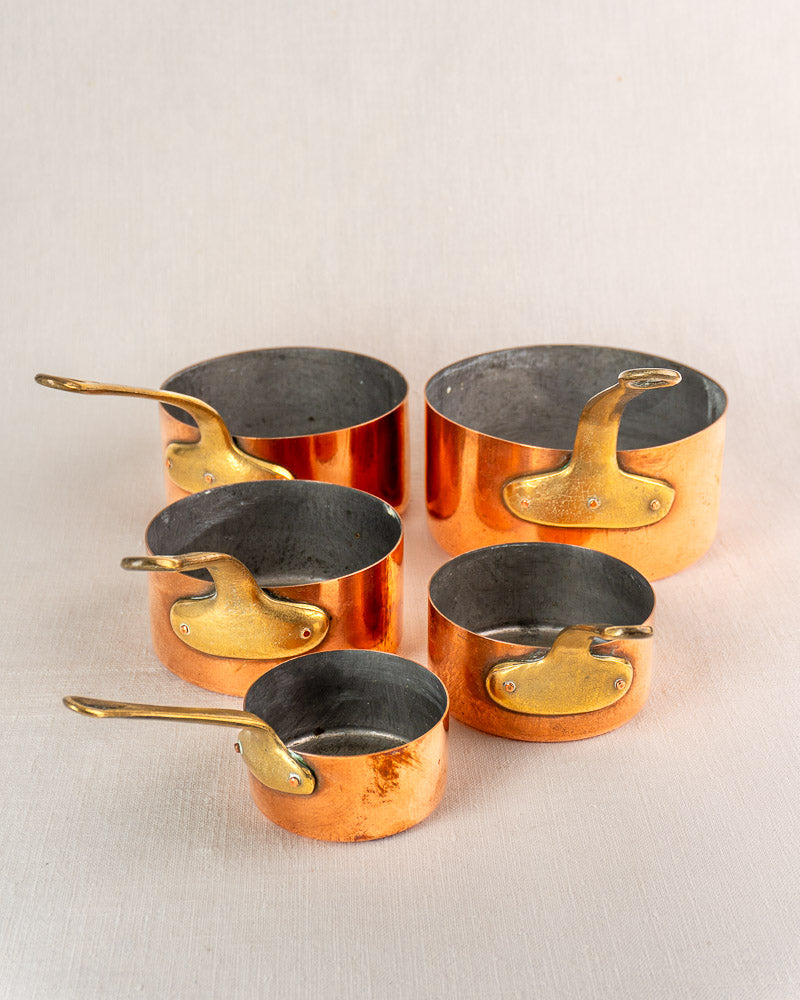 Antique French copper saucepan set of five with brass handles, early 20th century, on neutral surface.