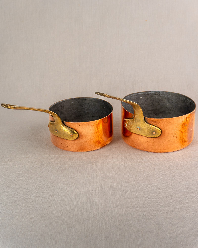 Set of five antique French copper saucepans with brass handles and tinned interiors, showcasing a classic rustic patina.