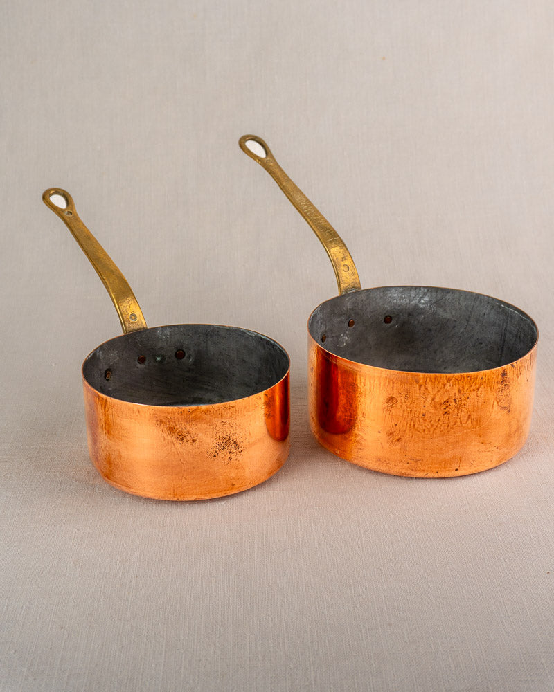 Antique French copper saucepan set of five with brass handles, early 20th century, on light neutral surface.