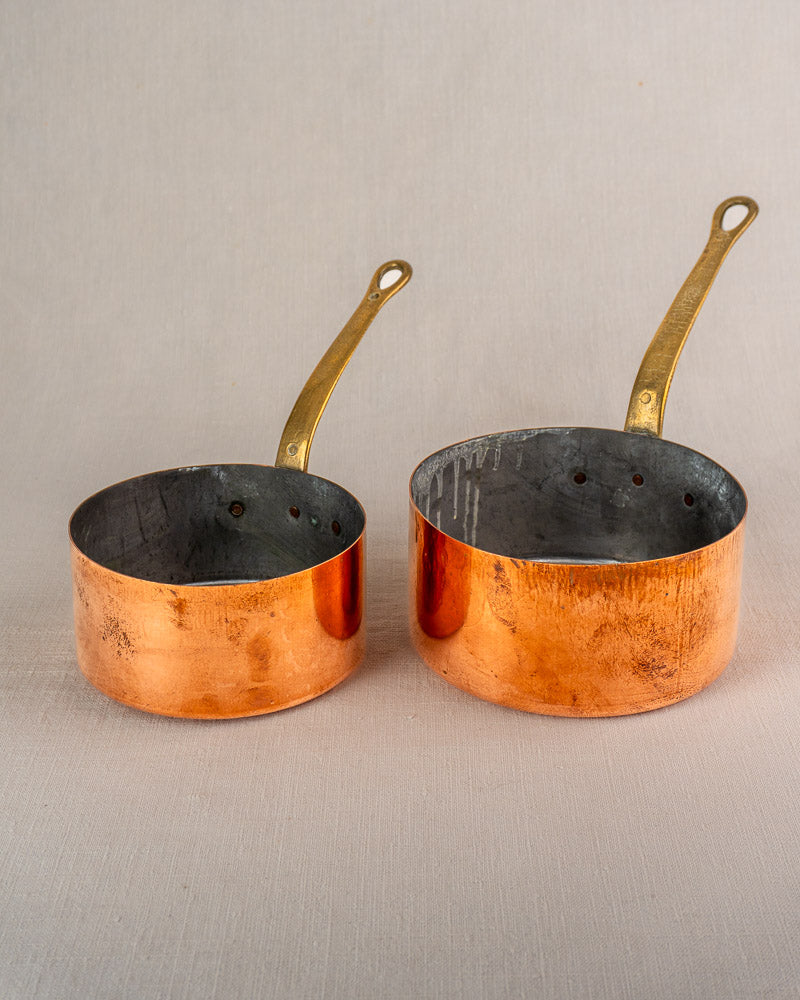 Set of five early 20th-century French antique copper saucepans with brass handles, visible wear and tarnish throughout.