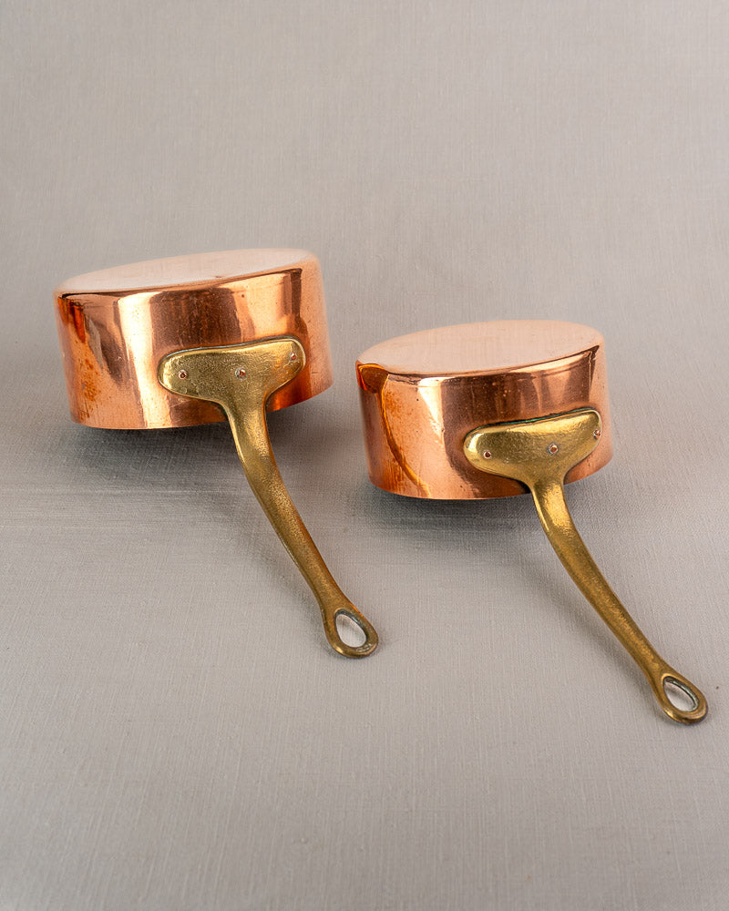 Antique French copper saucepan set of five with brass handles displayed upside down on a light gray surface.