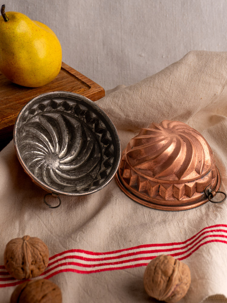 Antique French copper dessert molds with spiral relief, open on red-striped cloth, pear and walnuts nearby.